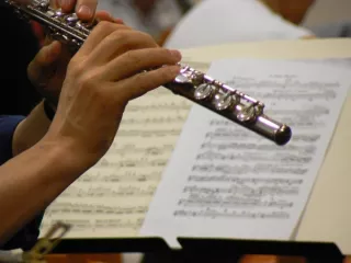 Close-up van hand met dwarsfluit, op de achtergrond bladmuziek